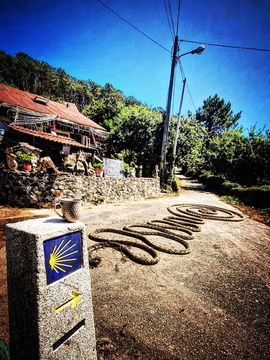 Una taza sobre un hito del Camino, con la palabra CAMINO formada con una cuerda